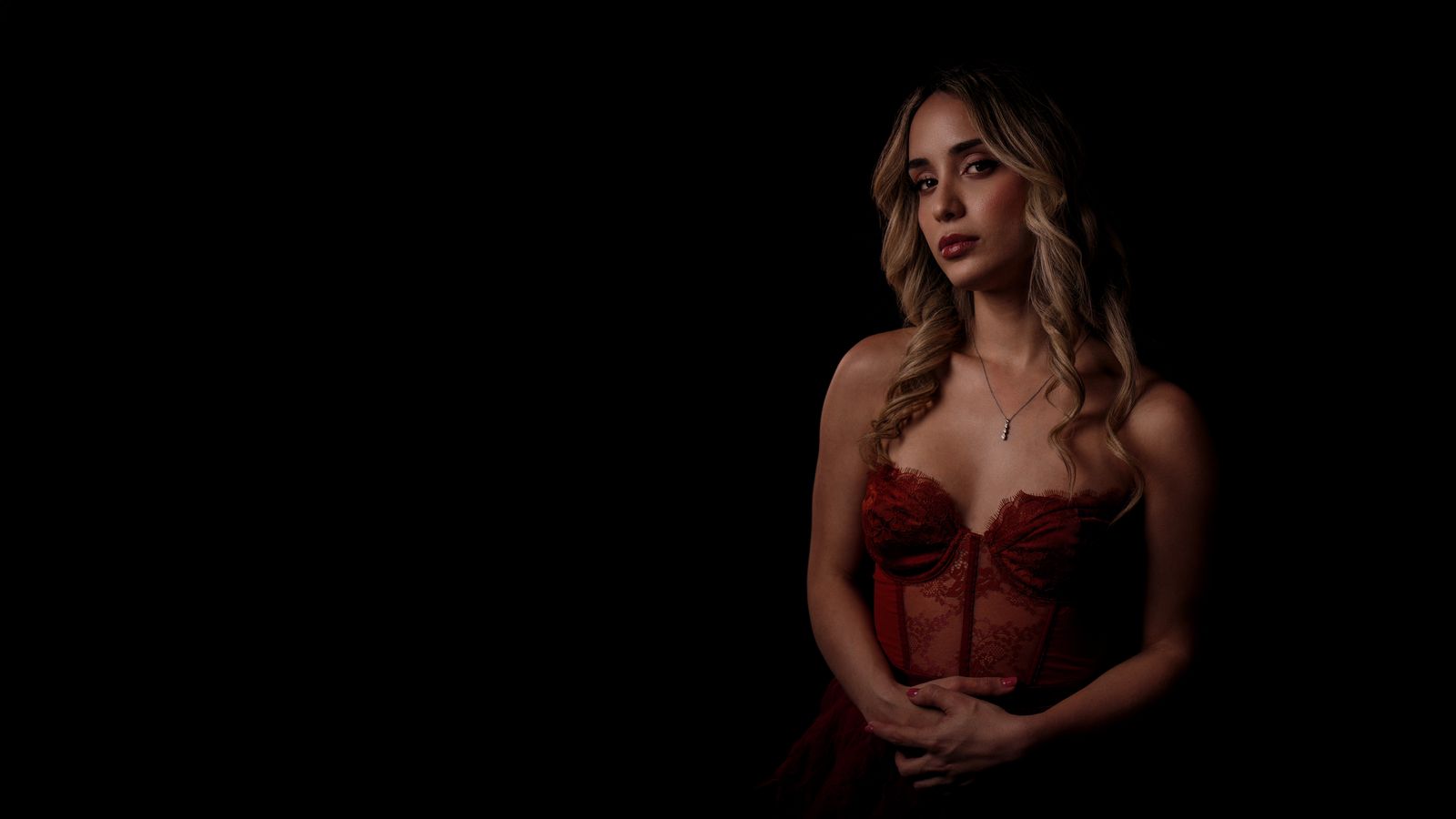 Raphaela in red lace against a black backdrop, looking at the camera, press photo, 2026.